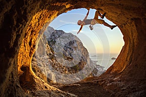 Young woman free solo climbing in cave with beautiful sea view in background