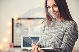 Young woman freelancer indoors home office concept winter atmosphere blurred background writing in planner smiling