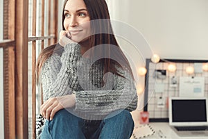 Young woman freelancer indoors home office concept winter atmosphere sitting on window sill