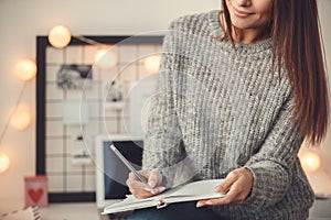 Young woman freelancer indoors home office concept winter atmosphere taking notes in planner close-up