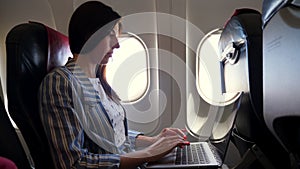 Young woman , freelancer works, using laptop while travelling by airplane. sitting near window in plane. work and travel