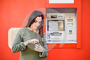 A young woman in front of an ATM searches her purse for some coins