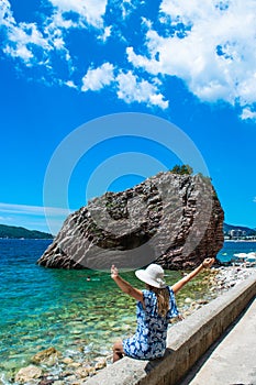 Young woman in front of beautiful rocks on pebble public stone beach. Rafailovici esort towns. Mountenegro