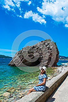 Young woman in front of beautiful rocks on pebble public stone beach. Rafailovici esort towns. Mountenegro