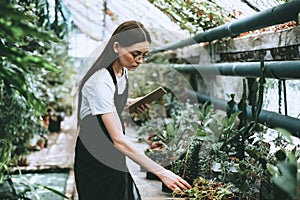 Young woman gardener in glasses with digital tablet working in a garden center