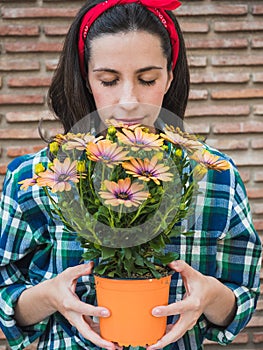 Young woman gardening at home holding pot with flowers
