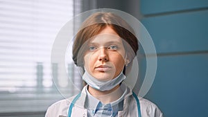 Young woman general practitioner looks straight against blue hospital room wall