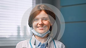 Young woman general practitioner looks straight against blue hospital room wall