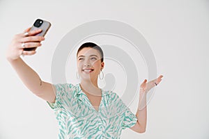 Young woman gesturing and taking selfie photo on cellphone