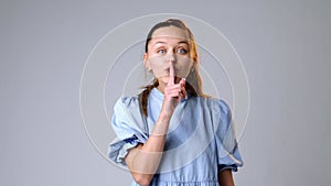 Young woman gesturing to keep calm and hush on gray background