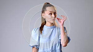 Young woman gesturing to keep calm and hush on gray background