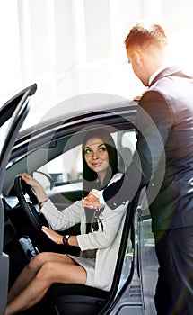 Young woman gets the key and smiling, sitting in a new car in the showroom.