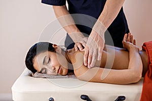 A young woman gets a massage procedure. Masseur makes back massage.