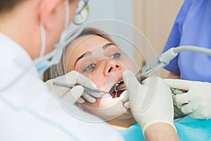 Young woman getting dental treatment closeup, hands of dentist and assistant makes treatment procedures to female