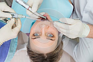 Young woman getting dental treatment closeup, hands of dentist and assistant makes treatment procedures to female