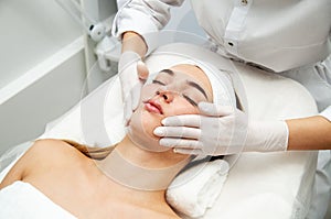 Young woman getting facial beauty treatment. Beautician cleaning and touching face