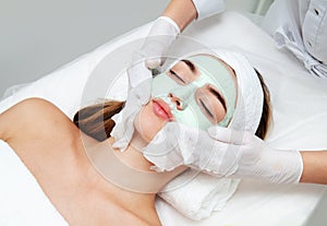 Young woman getting facial beauty treatment. Beautician cleaning and touching female face after facial mask