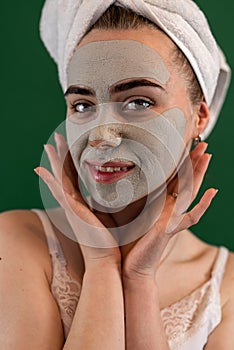 young woman getting green clay facial mask for skin care isolated on green