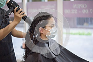 A young woman is getting a haircut in a hair salon , wearing face mask for protection covid-19 , salon safety concept