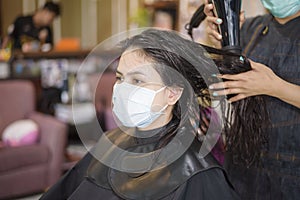 A young woman is getting a haircut in a hair salon , wearing face mask for protection covid-19 , salon safety concept