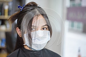 A young woman is getting a haircut in a hair salon , wearing face mask for protection covid-19 , salon safety concept
