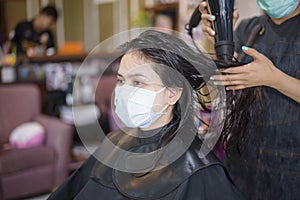 A young woman is getting a haircut in a hair salon , wearing face mask for protection covid-19 , salon safety concept