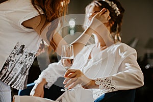 Young woman getting her makeup professionally done while she holds a glass of champagne.