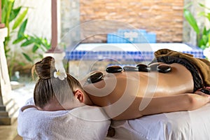 Young woman getting hot stone massage in spa salon. Beauty treat