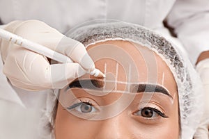 Young woman getting prepared for procedure of permanent eyebrow makeup in tattoo salon