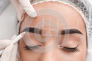 Young woman getting prepared for procedure of permanent eyebrow makeup in tattoo salon