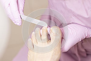 Young woman getting professional pedicure in a beauty salon, closeup. Hands a pedicurist in protective rubber gloves are applied w