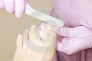 Young woman getting professional pedicure in a beauty salon, closeup. Hands a pedicurist in protective rubber gloves are applied w