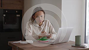 Young woman getting stressed over finances. Young woman looking worried over bills in kitchen. Working from home in