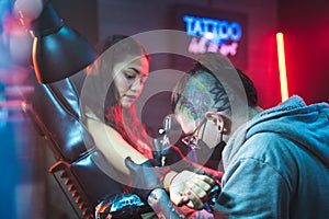 Young Woman Getting Tattoos In Beauty Parlor With Tattooist Working