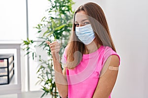 Young woman getting vaccine showing arm with band aid smiling happy and positive, thumb up doing excellent and approval sign