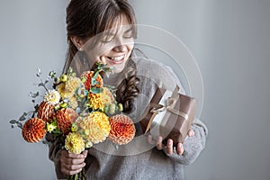 Young woman with a gift box and a bouquet of flowers in her hands.