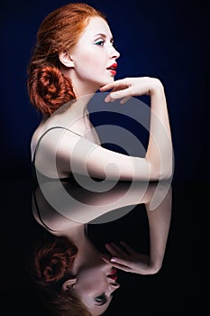 Young woman with ginger hair over reflection mirror on blue back