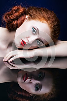 Young woman with ginger hair over reflection mirror on blue back