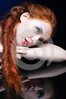 Young woman with ginger hair over reflection mirror on blue back