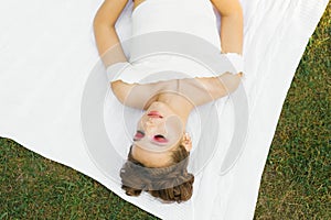 Young woman or girl with bright makeup and closed eyes is lying on a blanket on the lawn in the summer