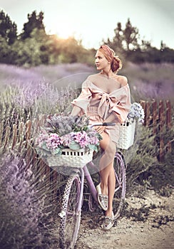 Young woman, girl in countryside, village stands at bicycle with flower baskets full of lavender and looks at field