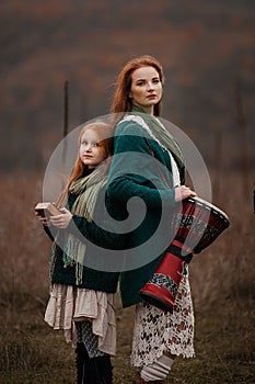 A young woman and a girl with red long hair playing kalimba and drum in the mountains in autumn