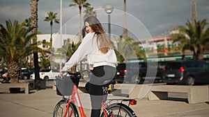 Young woman or girl riding bicycle pedalling next to palm trees