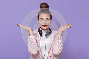 Young woman girl in rosy jacket posing isolated over lilac background, listen music, posing with headphones around neck, spreading