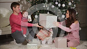 Young woman is giving christmas gifts to her husband, daughter and baby son.