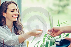 Young woman giving credit card to waiter hand and paying for coffee at cafe