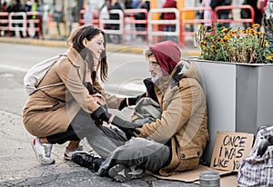 Young woman giving money to homeless beggar man sitting in city.