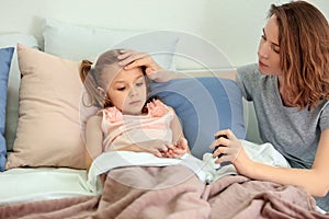 Young woman giving pill for her ill daughter in bed