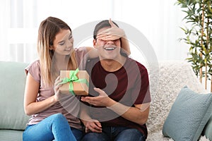 Young woman giving present to her beloved boyfriend at home