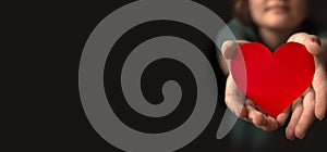 Young woman giving red heart. Concept of giving love. Healthcare, life insurance, mental health banner. Black background